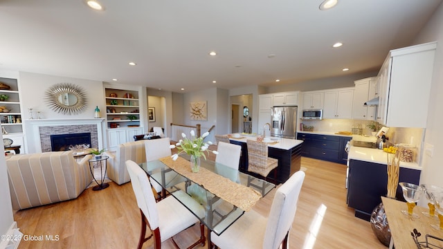 dining room with light wood finished floors, recessed lighting, a brick fireplace, and built in shelves