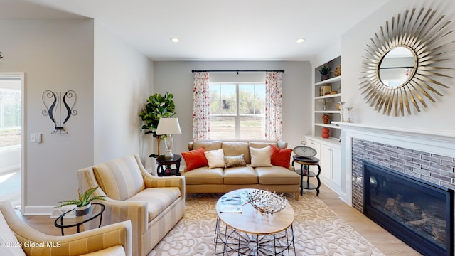 living room with light wood-type flooring, built in features, a glass covered fireplace, recessed lighting, and baseboards