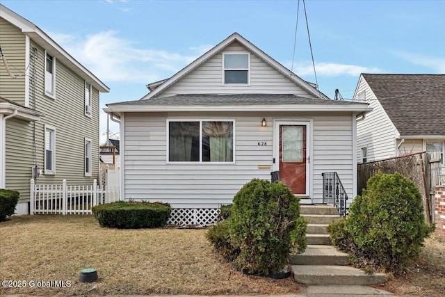 bungalow-style home featuring roof with shingles, a front lawn, and fence