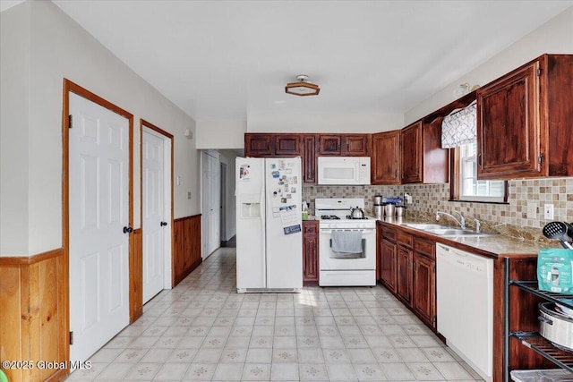 kitchen with white appliances, wooden walls, light floors, a sink, and wainscoting