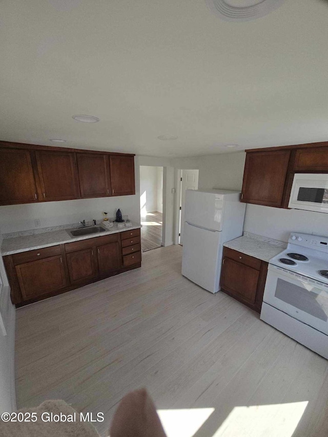 kitchen with a sink, light wood-type flooring, white appliances, and light countertops