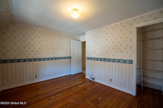 spare room featuring visible vents, ornamental molding, wood-type flooring, wallpapered walls, and baseboards