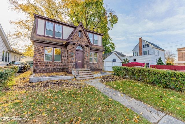 english style home with brick siding, a front yard, an outdoor structure, and fence