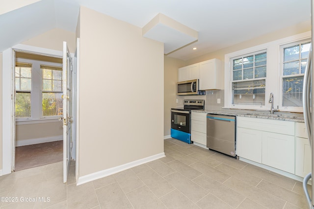 kitchen featuring light stone counters, a sink, stainless steel appliances, white cabinetry, and tasteful backsplash