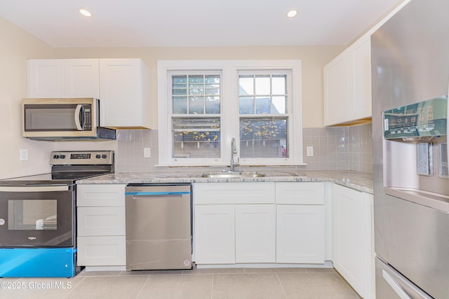 kitchen featuring light tile patterned floors, decorative backsplash, appliances with stainless steel finishes, white cabinetry, and a sink