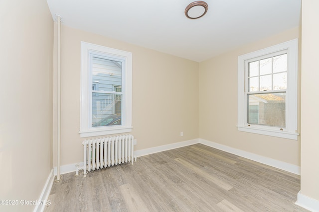 unfurnished room featuring radiator heating unit, baseboards, and wood finished floors