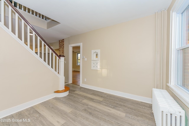 entrance foyer featuring radiator, baseboards, stairway, wood finished floors, and a baseboard radiator