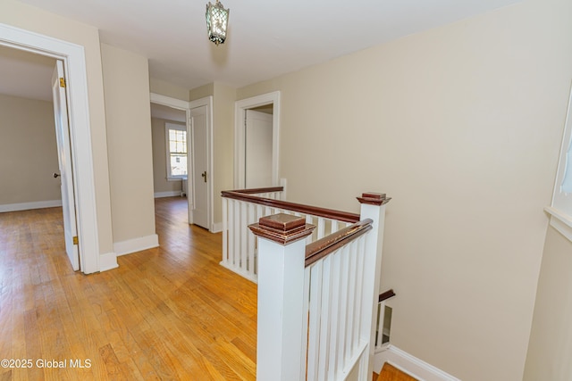 hall with light wood-style flooring, an upstairs landing, and baseboards