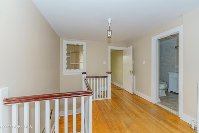 corridor featuring an upstairs landing, baseboards, and light wood finished floors