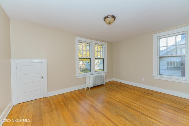 empty room featuring light wood finished floors, radiator heating unit, and baseboards