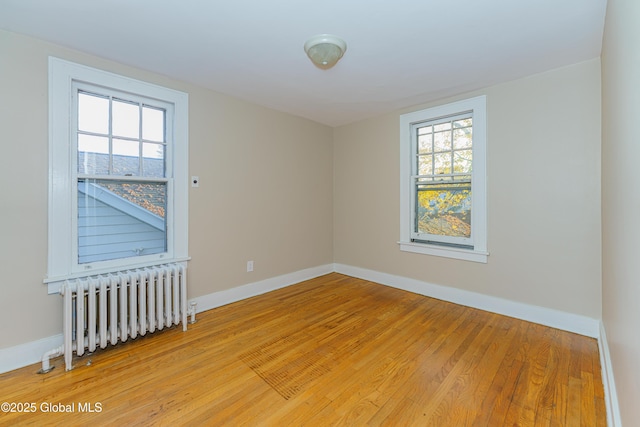 spare room featuring light wood-type flooring, baseboards, and radiator heating unit