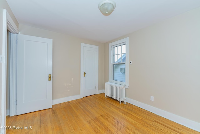 unfurnished bedroom featuring baseboards, radiator, and light wood finished floors