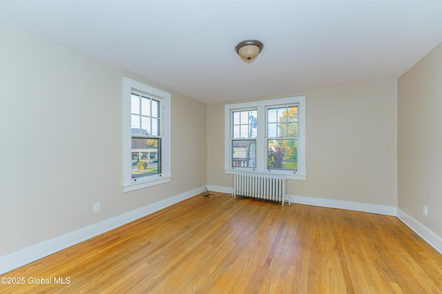 empty room with light wood-type flooring, baseboards, and radiator heating unit