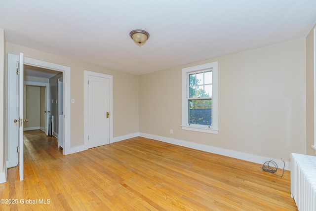 spare room with radiator, light wood-type flooring, and baseboards