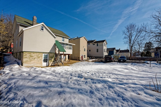 snow covered house featuring a chimney, stairs, and fence