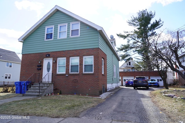 view of front of property with an outdoor structure, fence, brick siding, and driveway