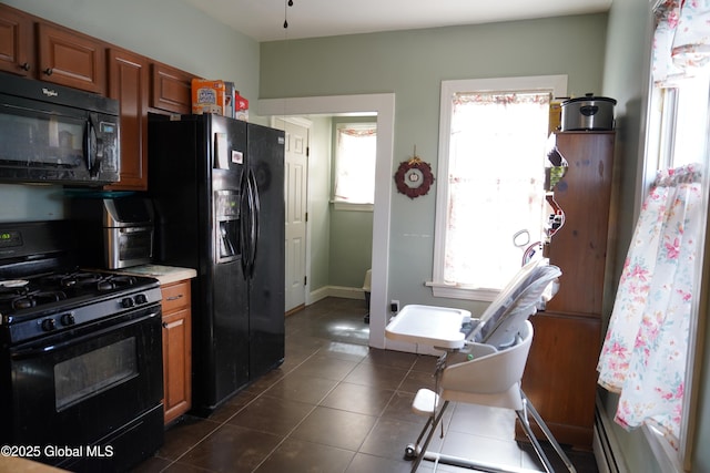 kitchen featuring brown cabinetry, baseboards, dark tile patterned flooring, black appliances, and light countertops
