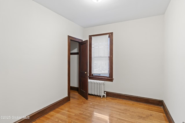 empty room with baseboards, radiator heating unit, and light wood-style floors