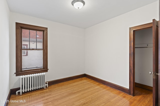 spare room featuring light wood finished floors, radiator, and baseboards