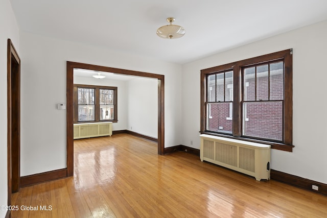 spare room with light wood finished floors, plenty of natural light, and radiator heating unit