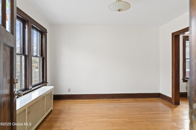 spare room with light wood-type flooring, baseboards, and radiator