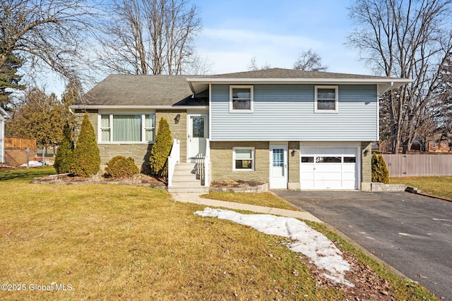 tri-level home with brick siding, a front lawn, fence, aphalt driveway, and a garage