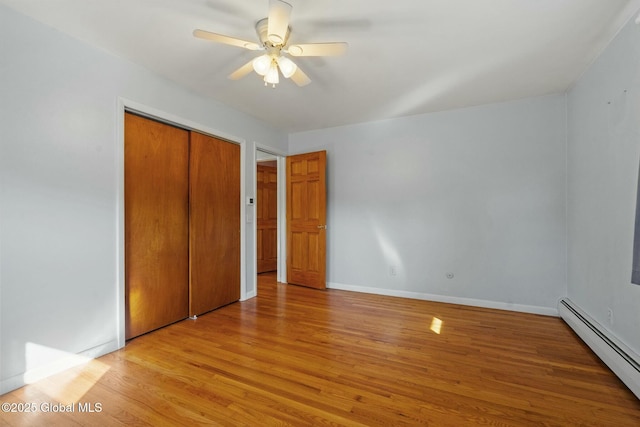 unfurnished bedroom featuring light wood-style flooring, a baseboard heating unit, a closet, baseboards, and ceiling fan