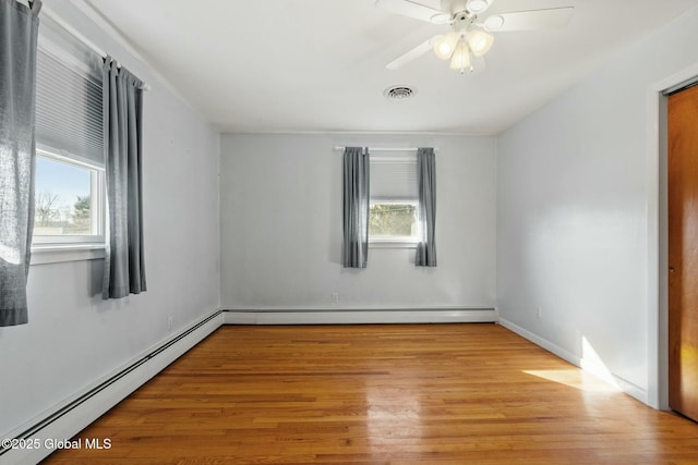 unfurnished room featuring a wealth of natural light, visible vents, wood finished floors, and a baseboard heating unit