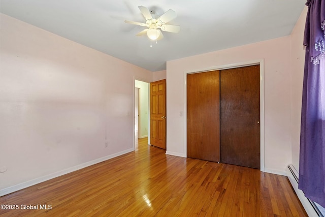 unfurnished bedroom with a closet, baseboard heating, light wood-style flooring, and baseboards