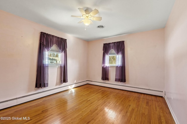 spare room featuring a wealth of natural light, visible vents, wood finished floors, and a baseboard heating unit