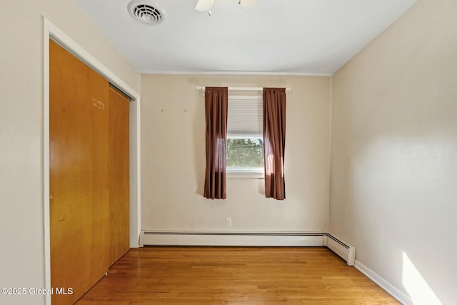 unfurnished room featuring visible vents, wood finished floors, and a baseboard heating unit