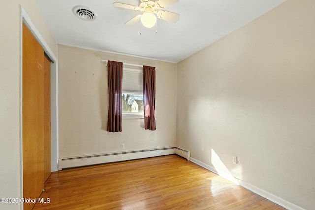 empty room featuring light wood-type flooring, visible vents, a ceiling fan, a baseboard heating unit, and baseboards