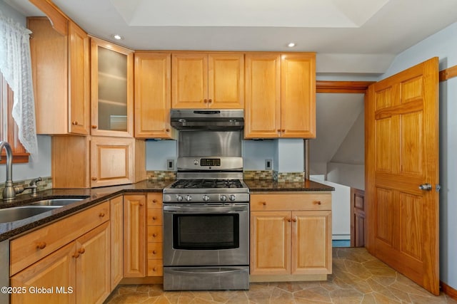 kitchen featuring glass insert cabinets, under cabinet range hood, dark stone countertops, stainless steel gas range, and a sink