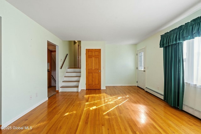 spare room featuring baseboards, stairs, a baseboard heating unit, and light wood-style floors