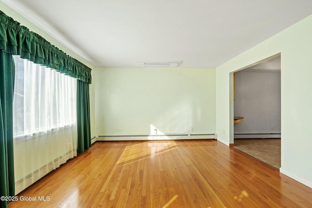 empty room featuring a baseboard heating unit, wood finished floors, visible vents, and baseboard heating