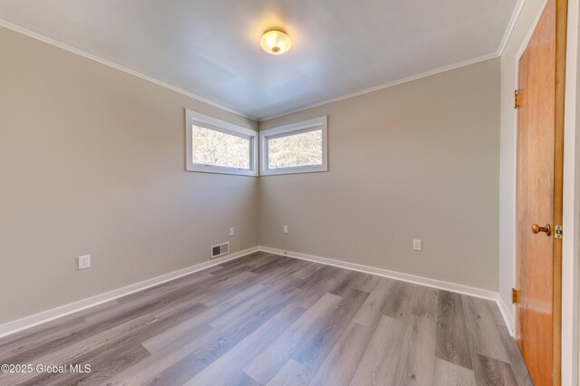 spare room featuring wood finished floors, crown molding, baseboards, and visible vents