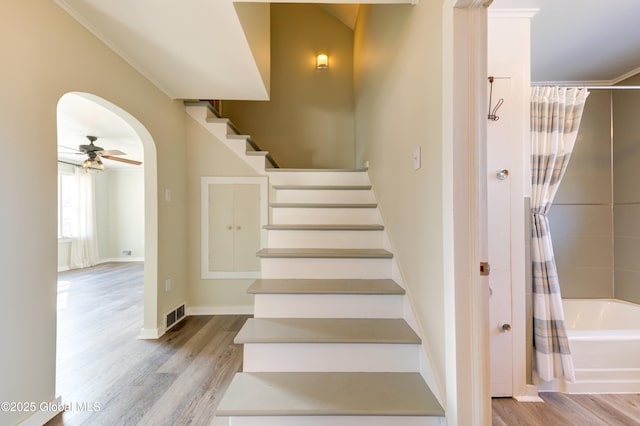 stairs with visible vents, baseboards, wood finished floors, arched walkways, and a ceiling fan