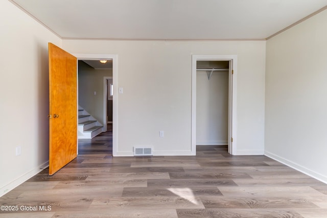 unfurnished bedroom featuring wood finished floors, visible vents, baseboards, a closet, and crown molding