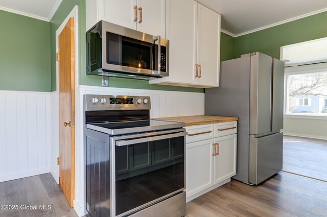 kitchen featuring crown molding, wainscoting, appliances with stainless steel finishes, wood finished floors, and white cabinets