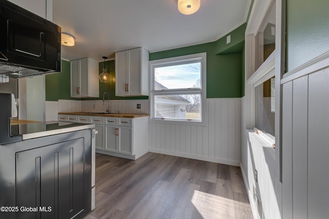 kitchen with a wainscoted wall, butcher block counters, wood finished floors, black appliances, and a sink