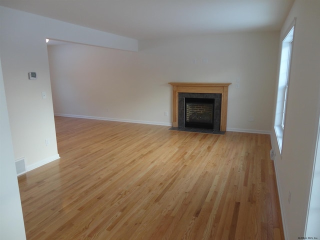 unfurnished living room with a tiled fireplace, baseboards, visible vents, and light wood-type flooring