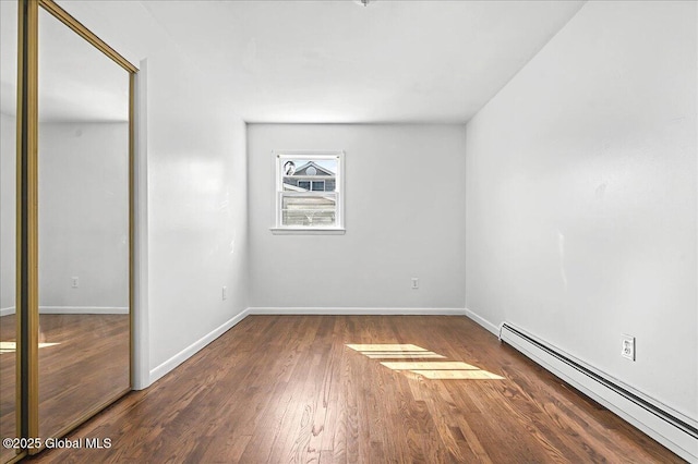 unfurnished bedroom with a baseboard heating unit, baseboards, a closet, and wood finished floors