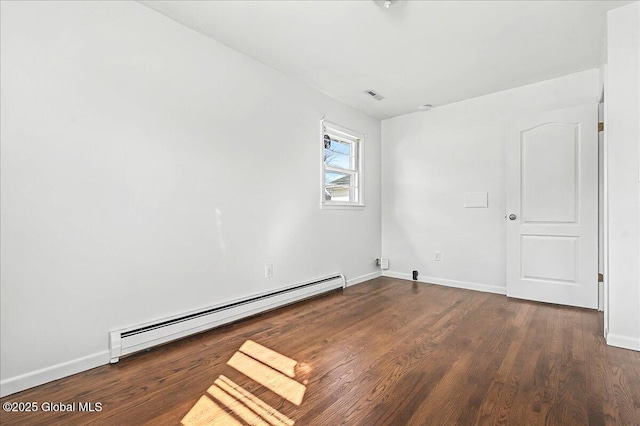 spare room featuring a baseboard heating unit, wood finished floors, visible vents, and baseboards