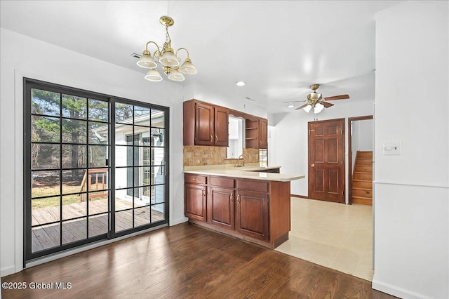 kitchen featuring dark wood finished floors, a peninsula, a sink, light countertops, and backsplash