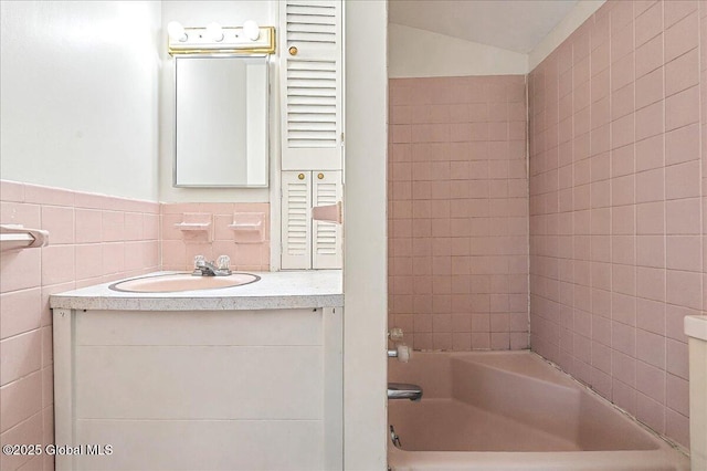 bathroom with tile walls, wainscoting, bathing tub / shower combination, vanity, and vaulted ceiling