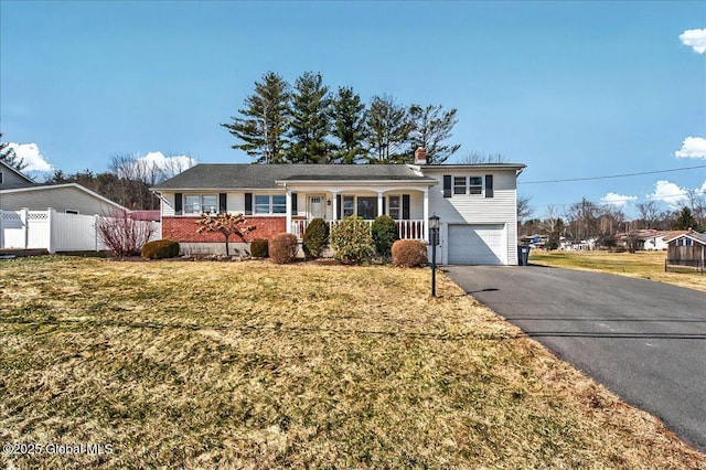 split level home featuring fence, aphalt driveway, a front yard, a chimney, and an attached garage