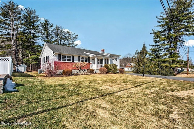 ranch-style house with brick siding, fence, a porch, a front yard, and an outbuilding