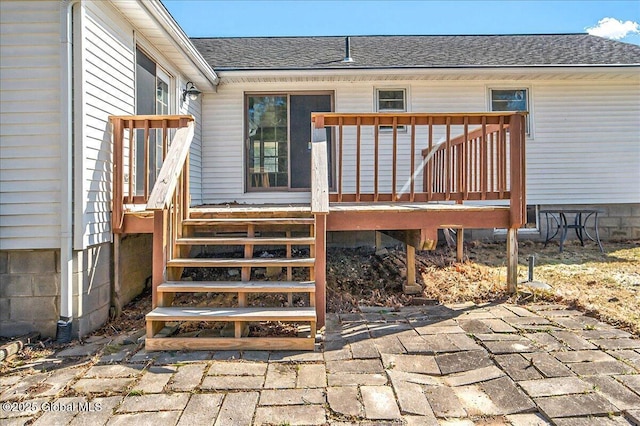 view of exterior entry featuring a deck and roof with shingles