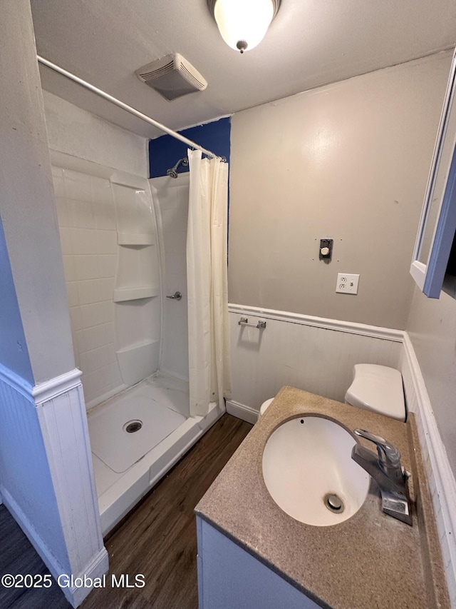 bathroom with a wainscoted wall, a shower with curtain, visible vents, and wood finished floors