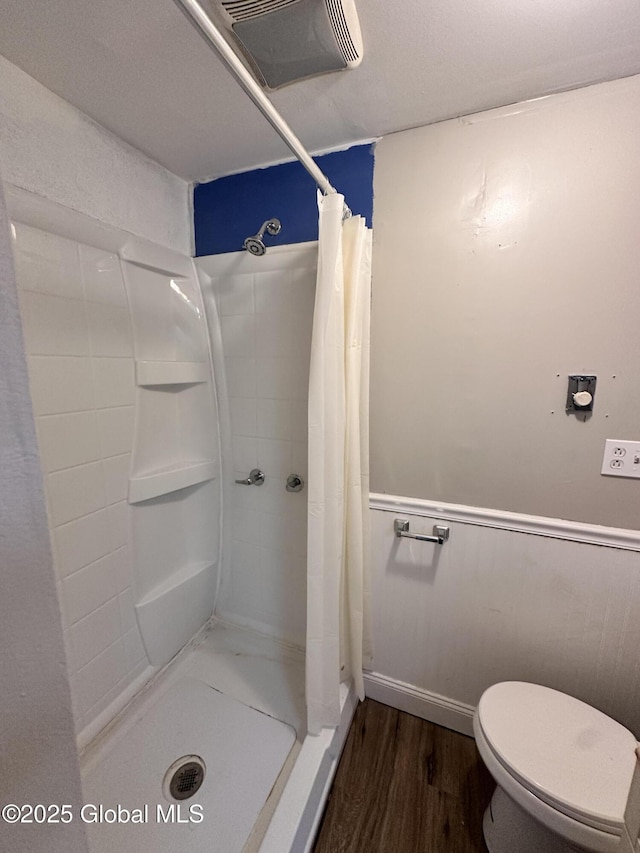 full bath with wood finished floors, toilet, a stall shower, and wainscoting